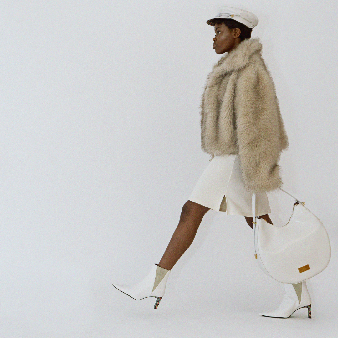 Model laufend mit Ensemble Yve aus Handtasche, Bakerboycap und Ankle Boots in creme 