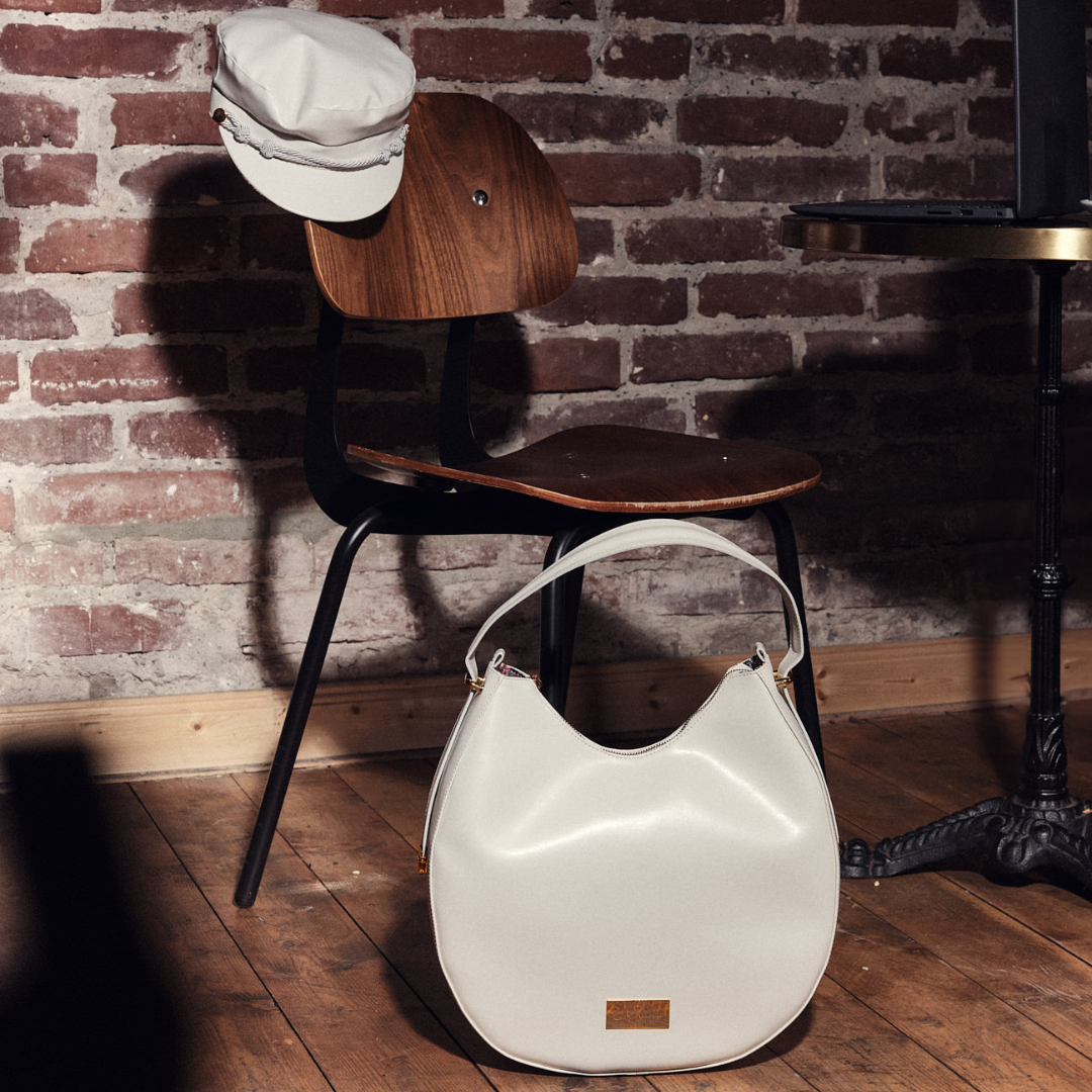 Yve Bag und Bakerboy Cap in creme auf einem Stuhl im Café