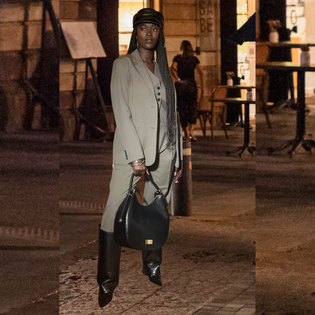 Model auf der Straße mit Ensemble Yve aus Handtasche, Bakerboycap und Highschaft Boots in schwarz